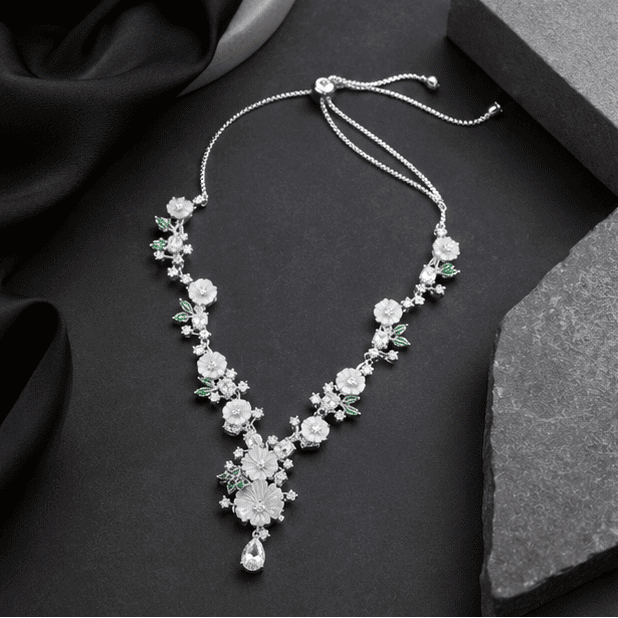 sterling silver floral necklace featuring white flower motifs, green leaf accents, and sparkling cubic zirconia on a black background.