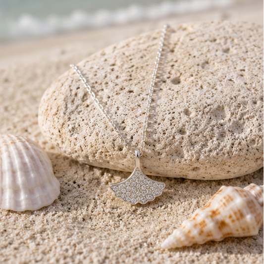 Beach-inspired sterling silver shell pendant necklace placed on soft coastal sand.