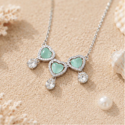  Beach-inspired flat lay of the Vrindae Argente Ocea Heart sterling silver necklace and earrings with mint green heart stones.